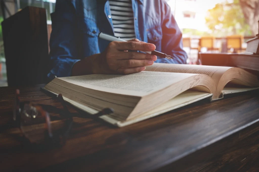 Man studying a book and taking notes with a pen at wooden desk